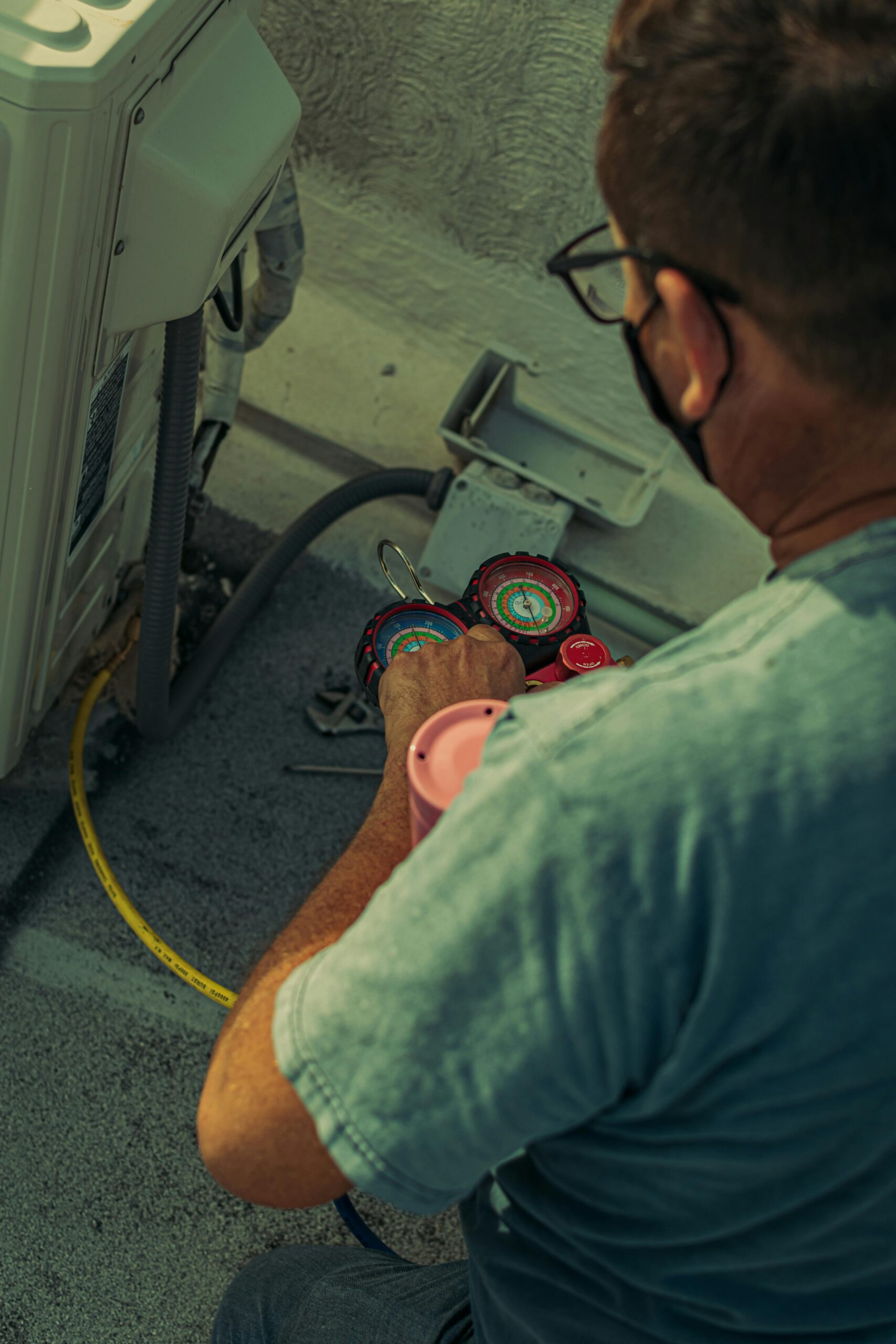 Home Professional technician repairing an outdoor air conditioning unit with gauges and tools.